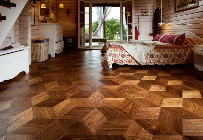 A cozy bedroom featuring intricate wooden parquet flooring and natural light streaming through open doors.